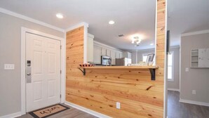 A hallway with a wooden accent wall, a white door, and a doormat with the word "Welcome". - Luxury Lake Martin Condo  (Dadeville)