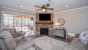 A living room with a stone fireplace, a ceiling fan, and a flat-screen TV mounted above it. - Luxury Lake Martin Condo  (Dadeville)