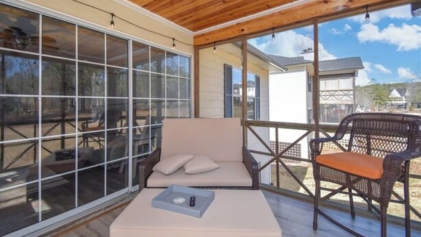 A covered patio with a sofa and wicker chairs, large windows, and a view of the surrounding area. - Luxury Lake Martin Condo  (Dadeville)