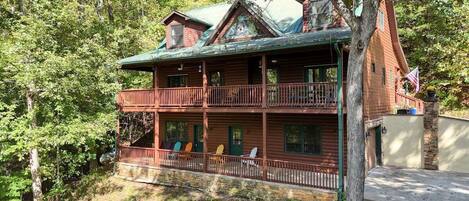 A two-story log cabin with a balcony, surrounded by dense forest.
