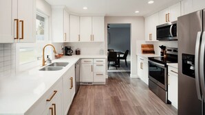 A modern kitchen with white cabinetry, stainless steel appliances, and wooden flooring.