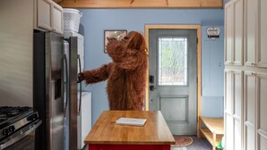 Une cuisine avec des meubles de rangement en bois, un réfrigérateur et une porte ornée d’une pancarte accueillante.