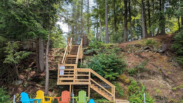 Un escalier en bois mène à une jetée où sont disposées des chaises Adirondack aux couleurs vives.