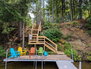Een houten trap die leidt naar een steiger met kleurrijke Adirondack-stoelen.