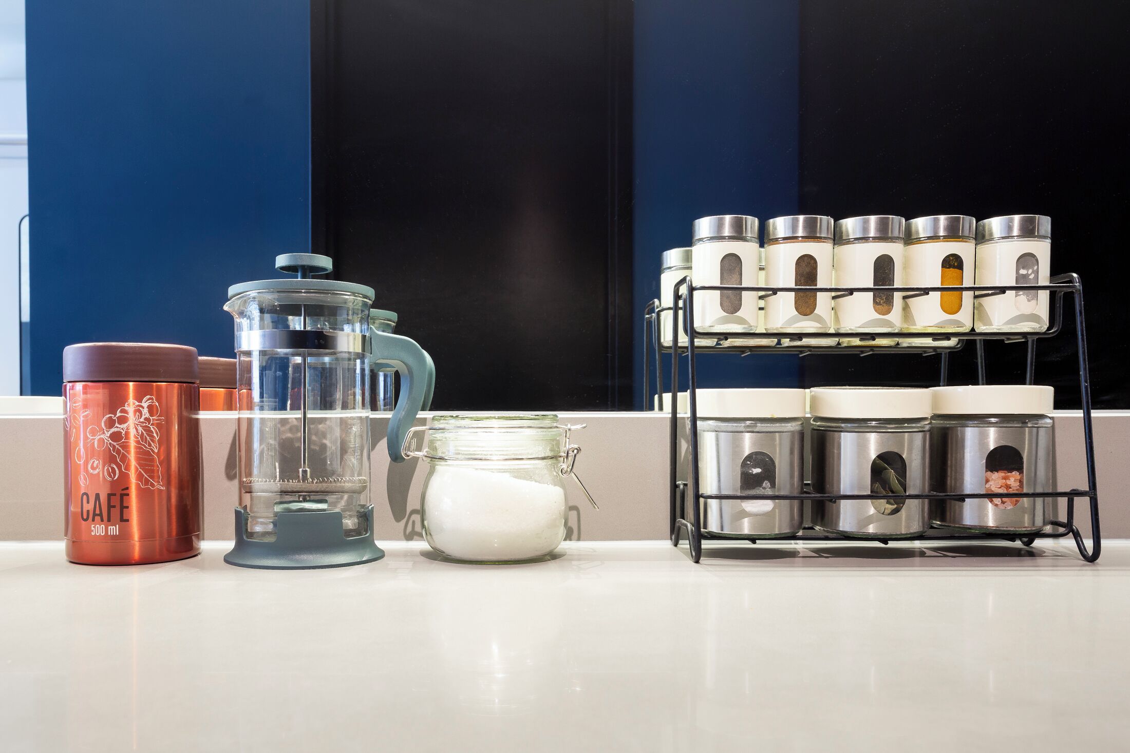 Un plan de travail de cuisine avec une machine à café, un thermos, un pot à sucre et un étagère à épices.