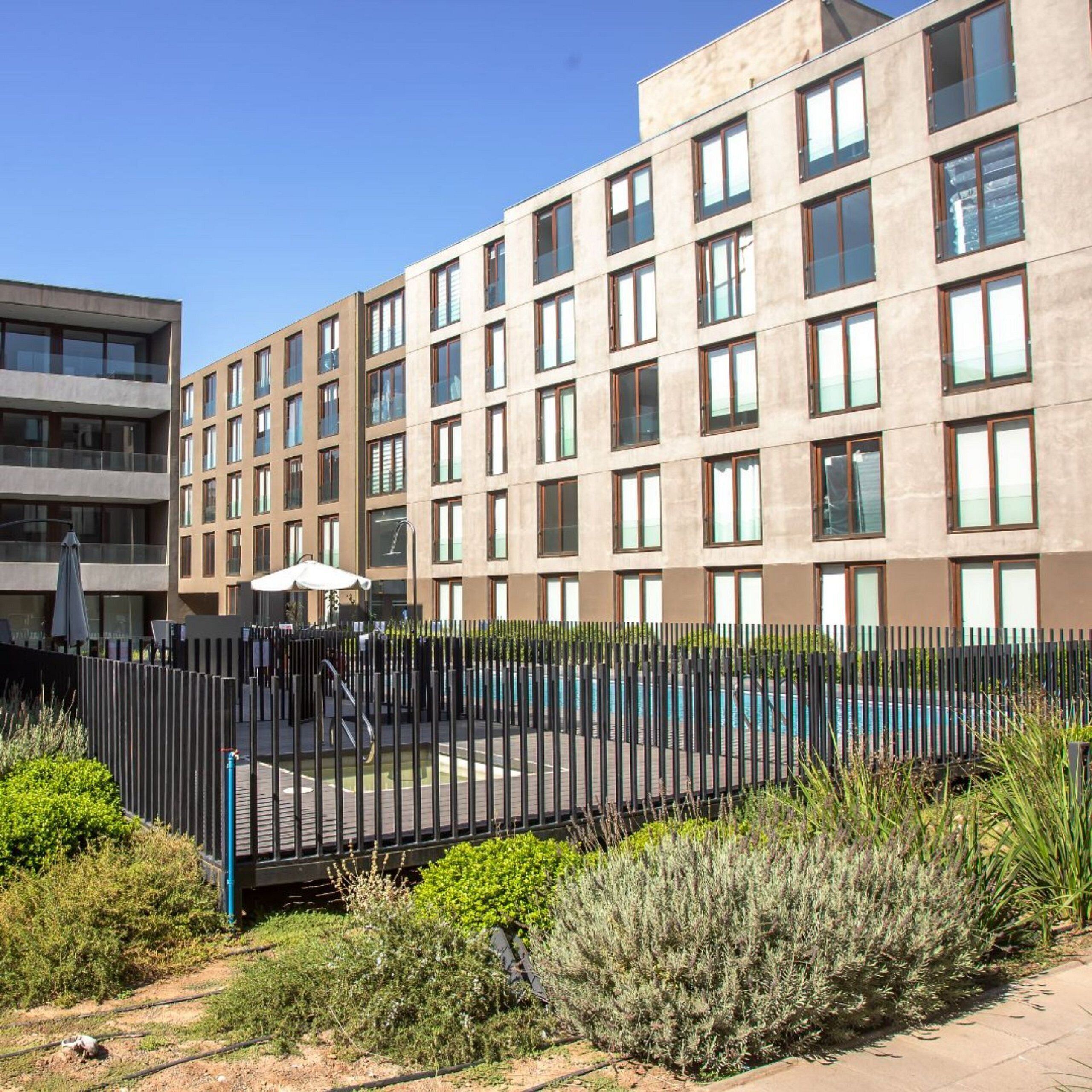 A modern building with multiple floors, large windows, and a fenced outdoor area with a pool.