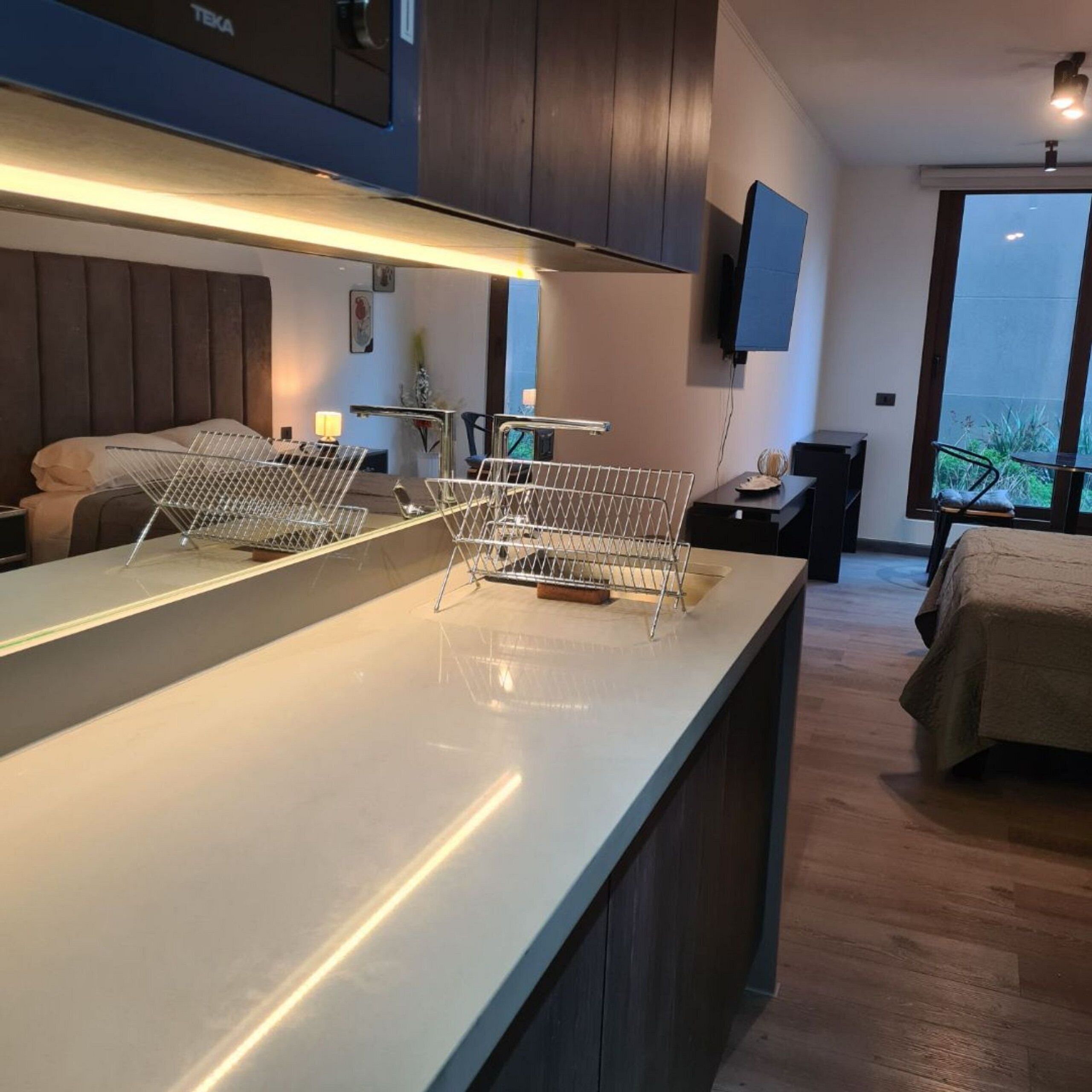 Een moderne keuken met een centraal eiland, een eethoek met tafel en stoelen, en een slaapkamer met bed en balkon.
