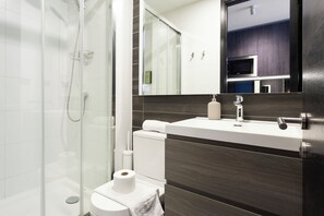 A modern bathroom with a glass shower enclosure, a toilet, and a sink with a mirror above.