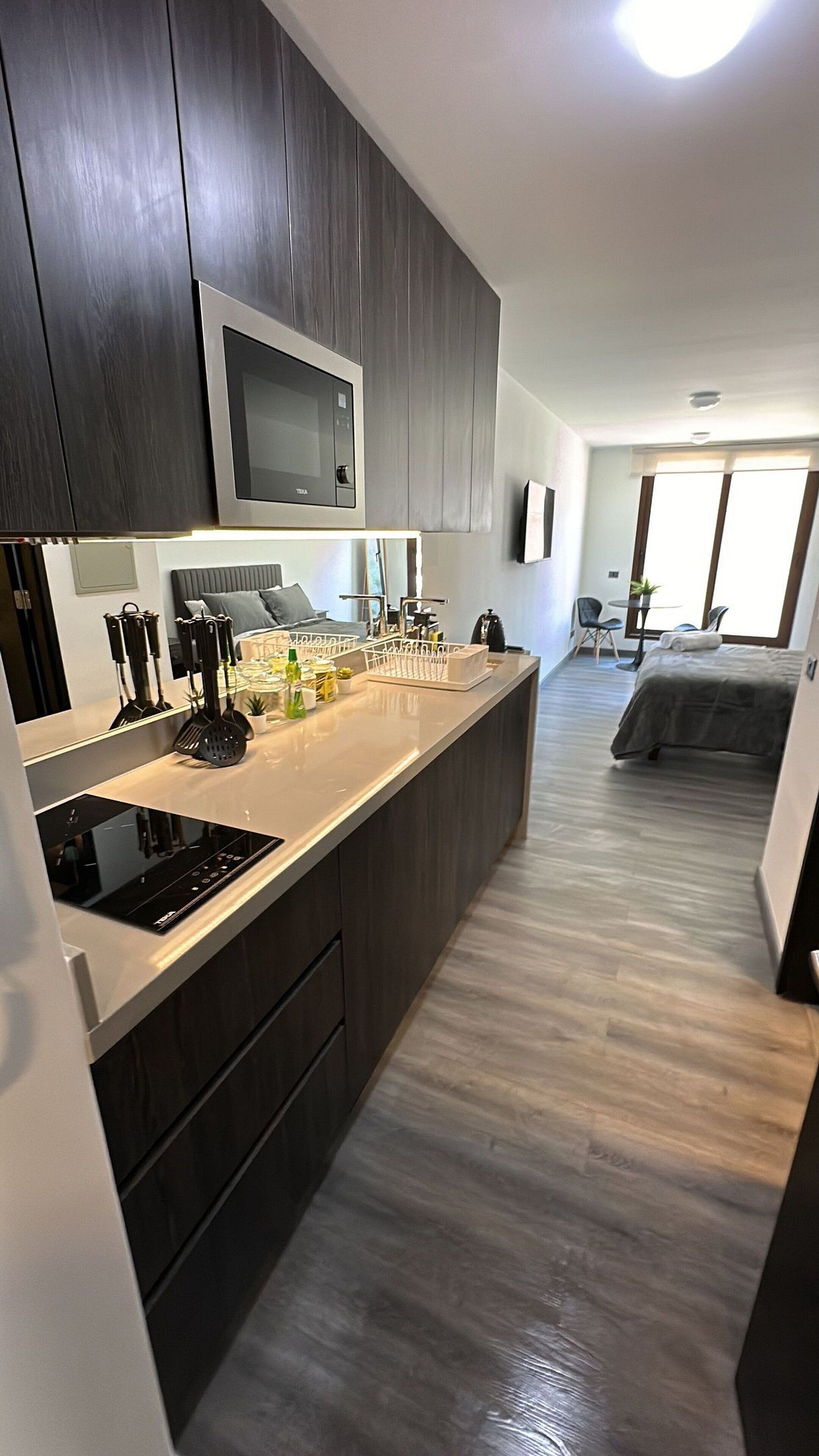 Una cocina moderna con armarios de madera oscura, microondas integrado y una isla central con utensilios de cocina.