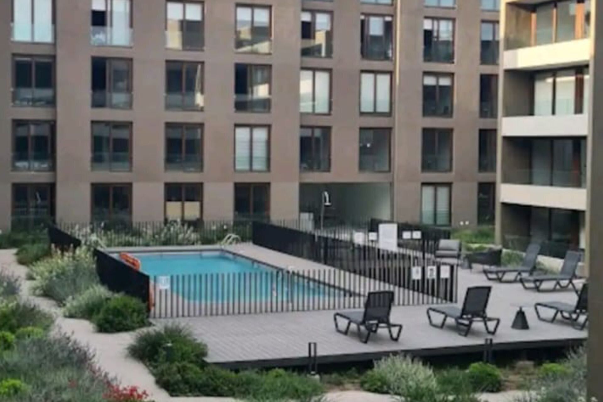 Ein modernes Gebäude mit Poolbereich auf dem Dach, einschließlich Liegestühlen und einem eingezäunten Pool.