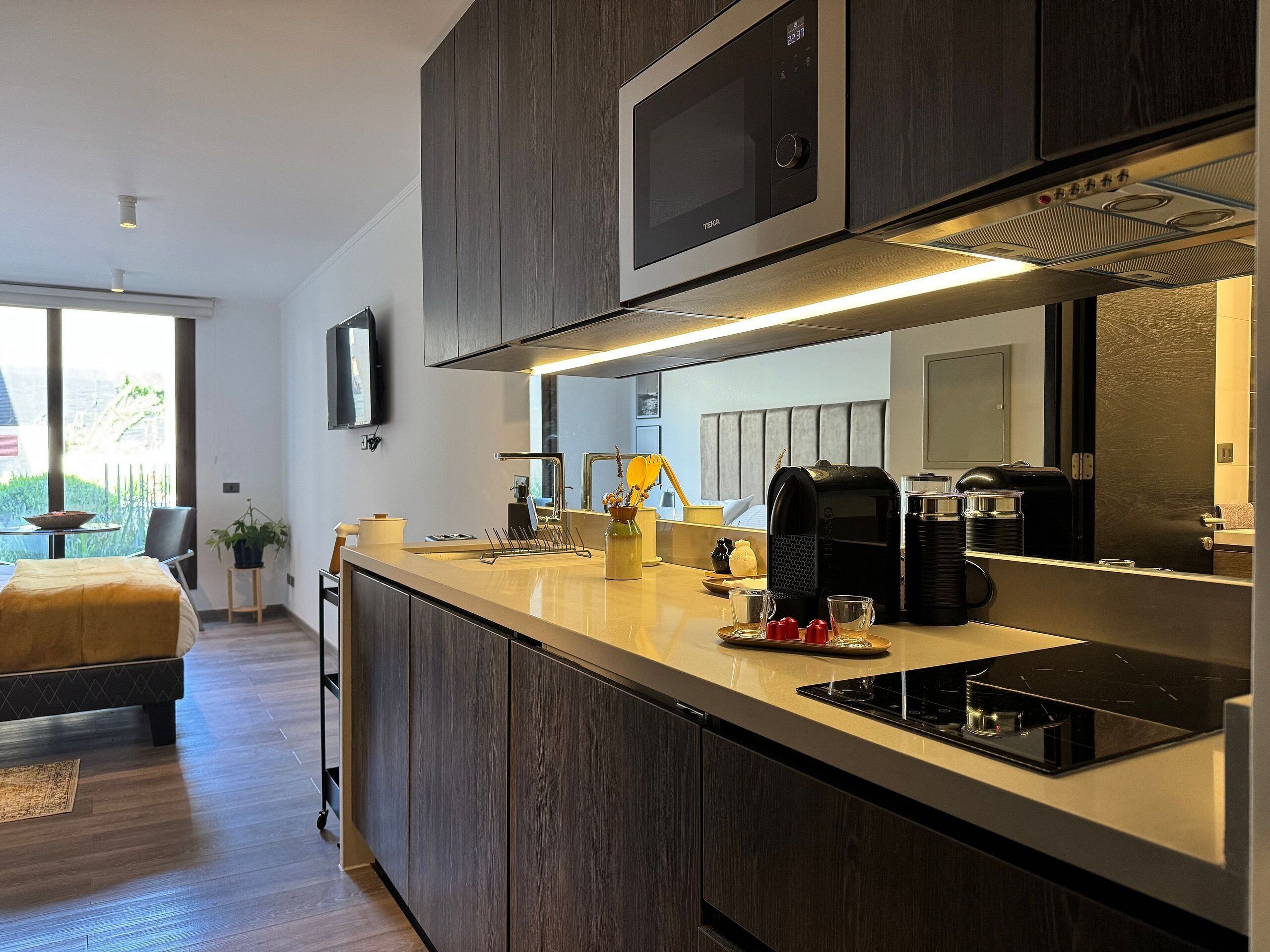 Una cocina moderna con microondas integrado, cafetera y un lavamanos pequeño.