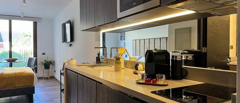 Una cocina moderna con microondas integrado, cafetera y un lavamanos pequeño.