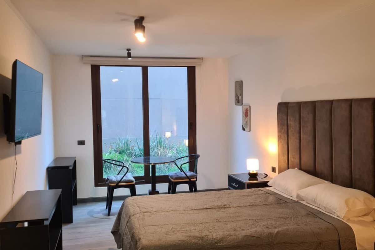 Quarto moderno com cama grande, escrivaninha, cadeira, televisão e varanda com vista.