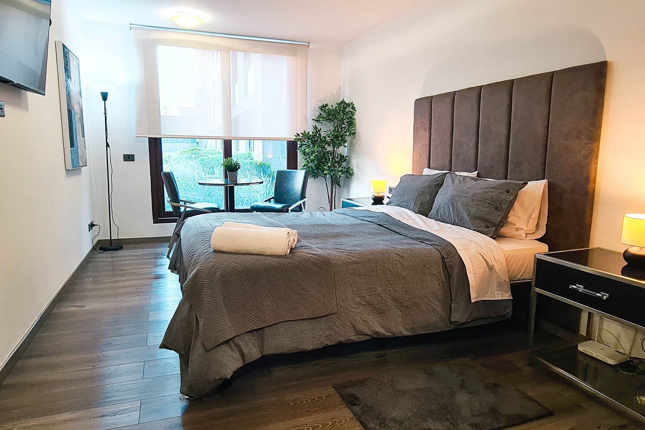 Een moderne hotelkamer met een groot bed, nachtkastje en uitzicht op het omliggende landschap.