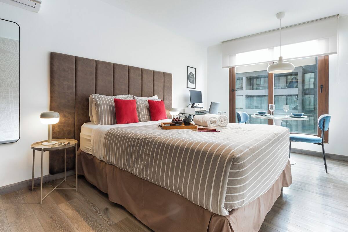 Quarto de hotel moderno com uma cama grande, uma escrivaninha e um espaço de refeições com cadeiras.