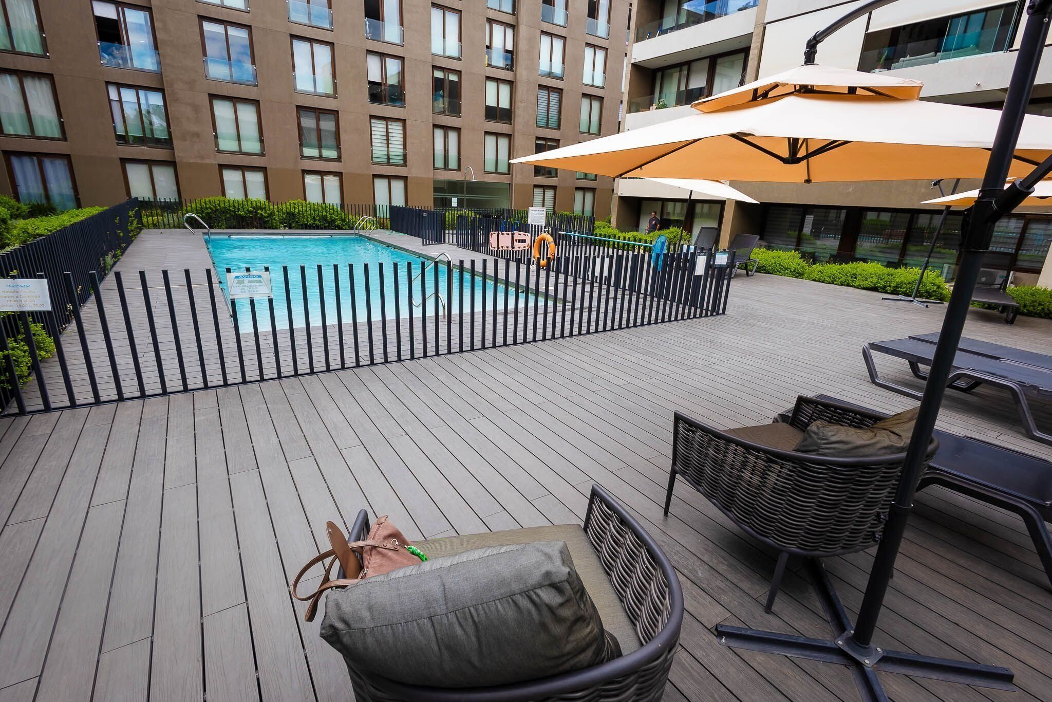 A pool area with a wooden deck, lounge chairs, and umbrellas.