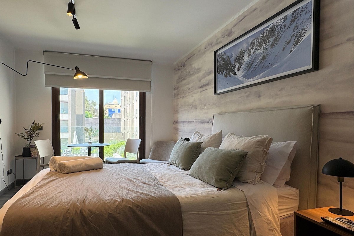 Quarto moderno com uma cama grande, vista da cidade pela janela e um quadro na parede.