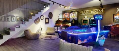 A modern living room with a gaming area featuring arcade machines, a staircase, and a comfortable seating area.