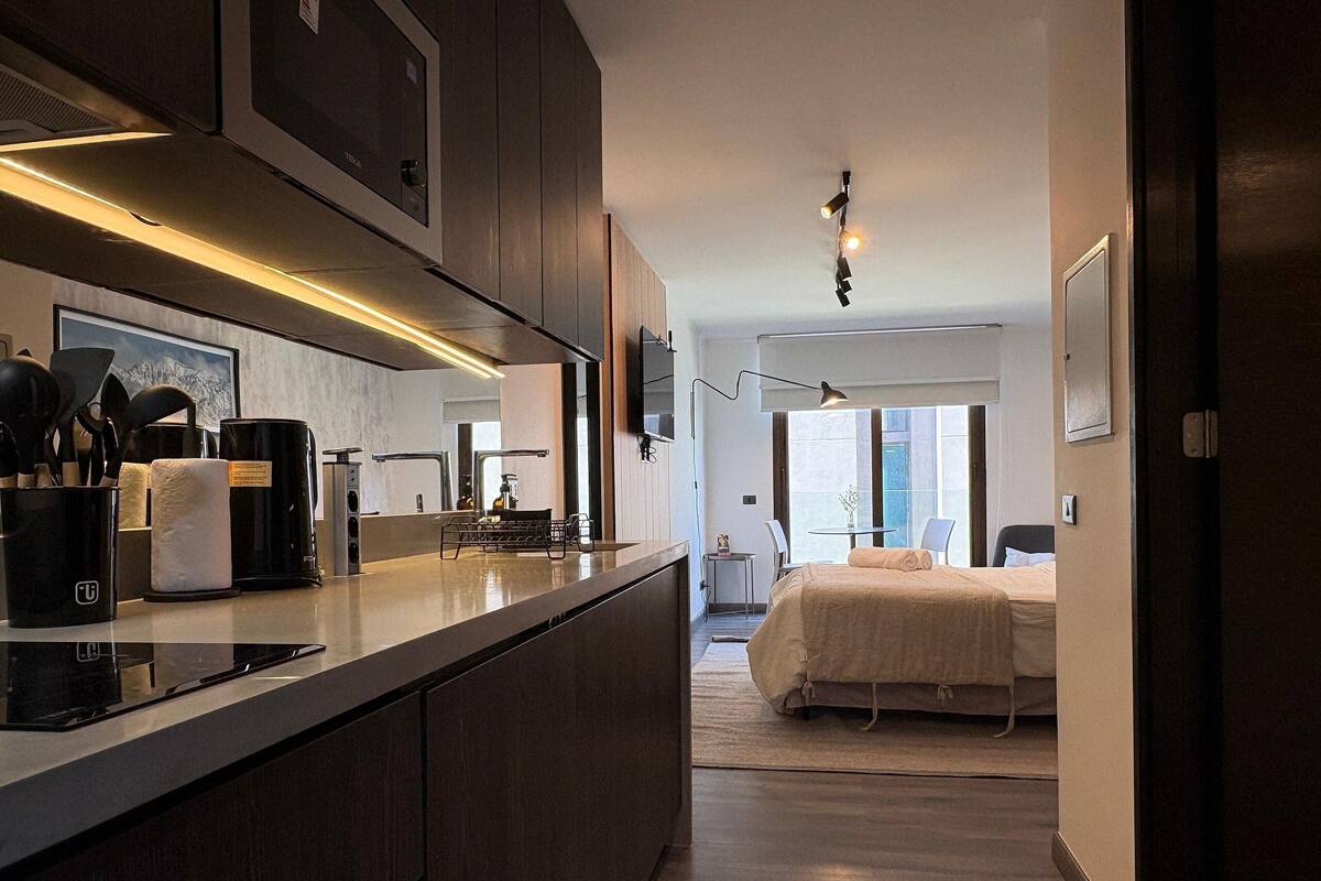 Uma cozinha moderna com uma ilha central, uma sala de jantar com mesa e cadeiras, e um quarto com cama e janela.