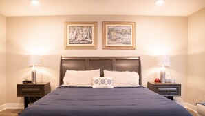 A neatly made bed with a dark blue bedspread and two pillows, flanked by two bedside tables with lamps and framed artwork on the wall above.