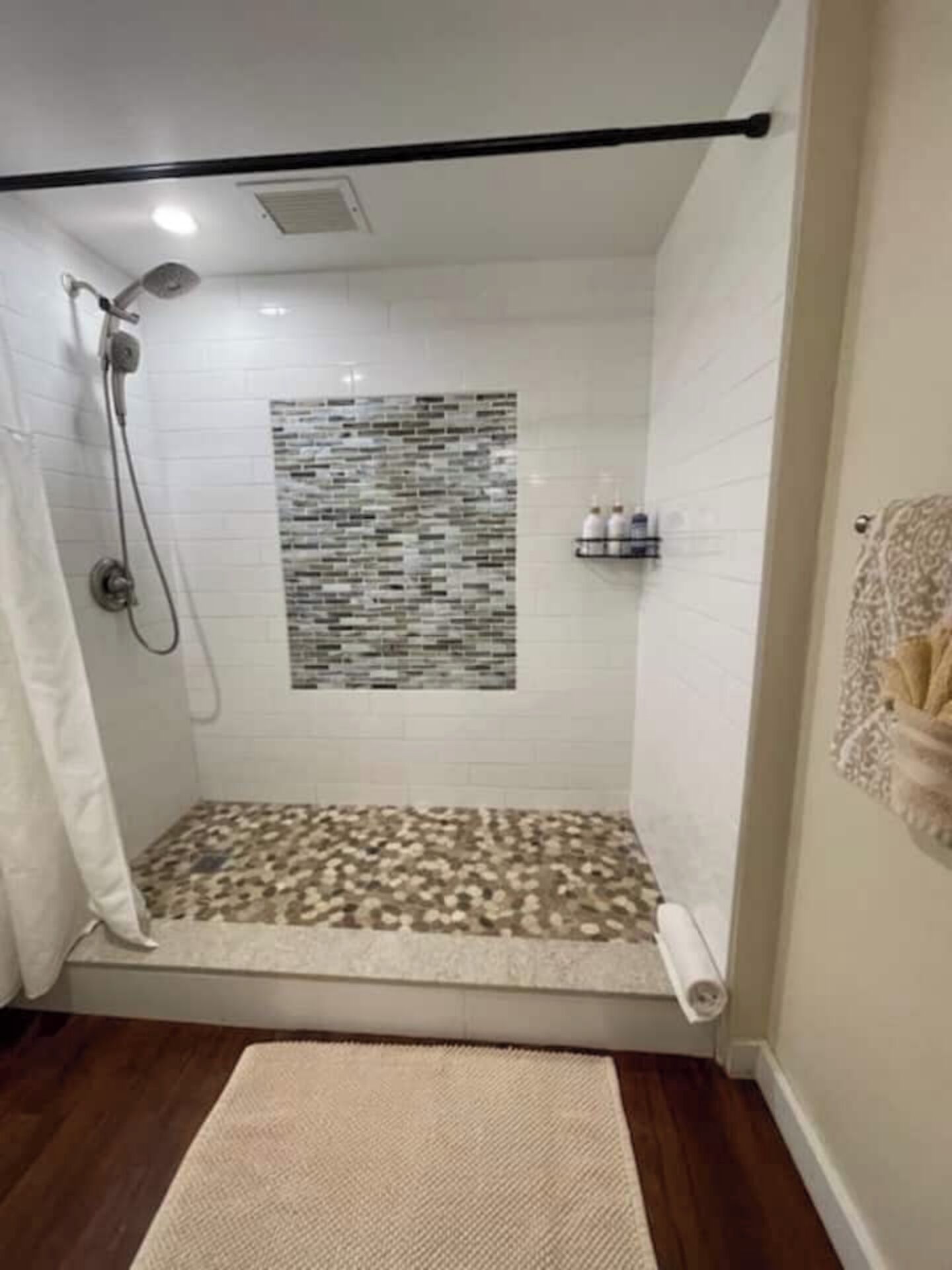 A shower area with a tiled floor, a showerhead, and a wall-mounted shelf with bottles.