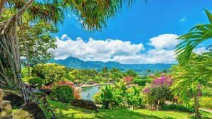 Um jardim exuberante com piscina, palmeiras e montanhas ao fundo.