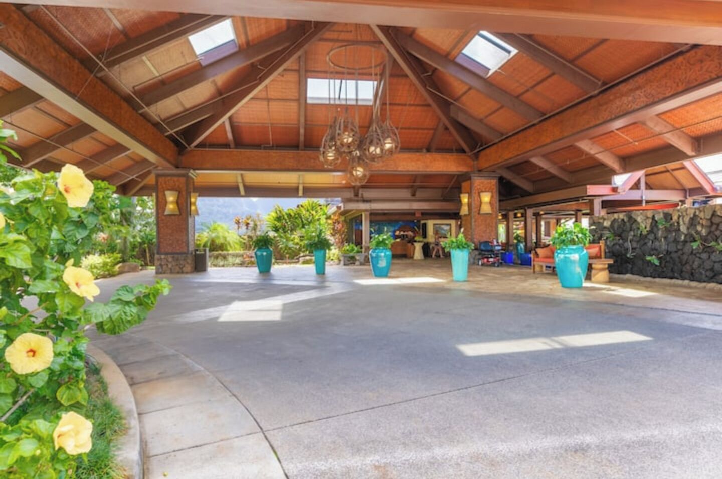 An outdoor covered area with a concrete floor, potted plants, and a wooden ceiling structure.