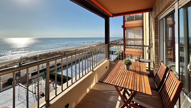Ein Balkon mit Holztisch und -stühlen mit Blick auf einen Strand und den Ozean.