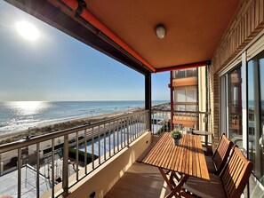 A balcony with a wooden table and chairs, overlooking a beach and the ocean. - Charming 2-bedroom apartment with AC, WiFi in lovely Mar y Naranjo (Mar y Naranjo)