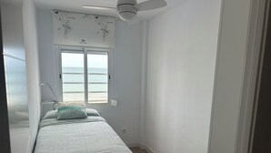 Ein Schlafzimmer mit Bett, Fenster mit Meerblick, Deckenventilator und einer Karte an der Wand.