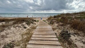 Ein hölzerner Steg führt zu einem Strand bei bedecktem Himmel.