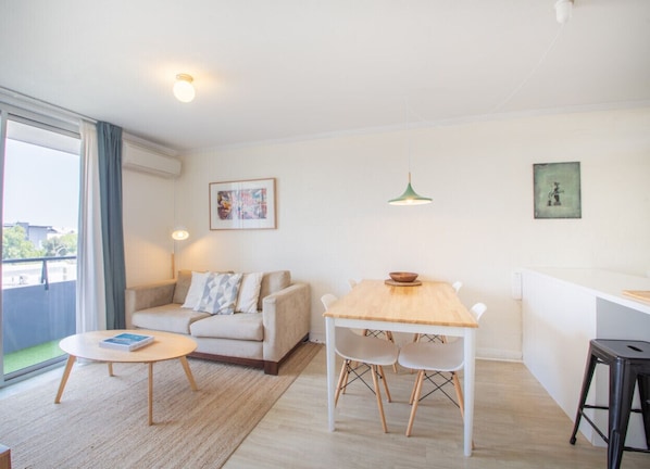 A modern living room with a sofa, a dining table, and a kitchen area.