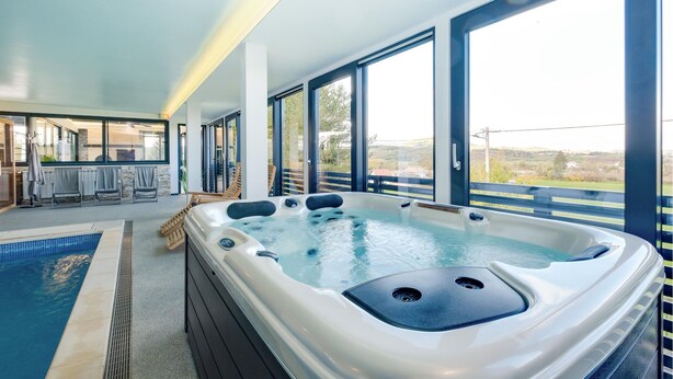 Een modern binnenzwembad met een jacuzzi, grote ramen en uitzicht op het landschap.