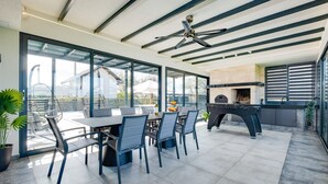 Een modern terras met eethoek, een tafel, stoelen, een plafondventilator en een uitzicht op de stad door grote ramen.