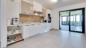 Een moderne keuken met witte kasten, een koffieapparaat en uitzicht op een balkon.