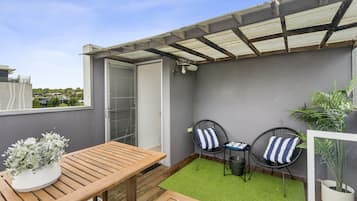 A patio area with a wooden table and two chairs, a small green rug, and a potted plant.