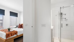 A modern bedroom with a bed, bedside table, and window with blinds.