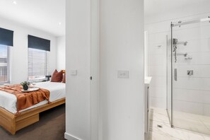 A modern bedroom with a bed, bedside table, and window with blinds. - The Red Ember Retreat (Caulfield North)