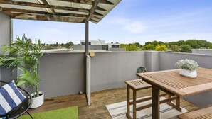 A rooftop patio with a wooden table and chairs, a potted plant, and a view of the cityscape.