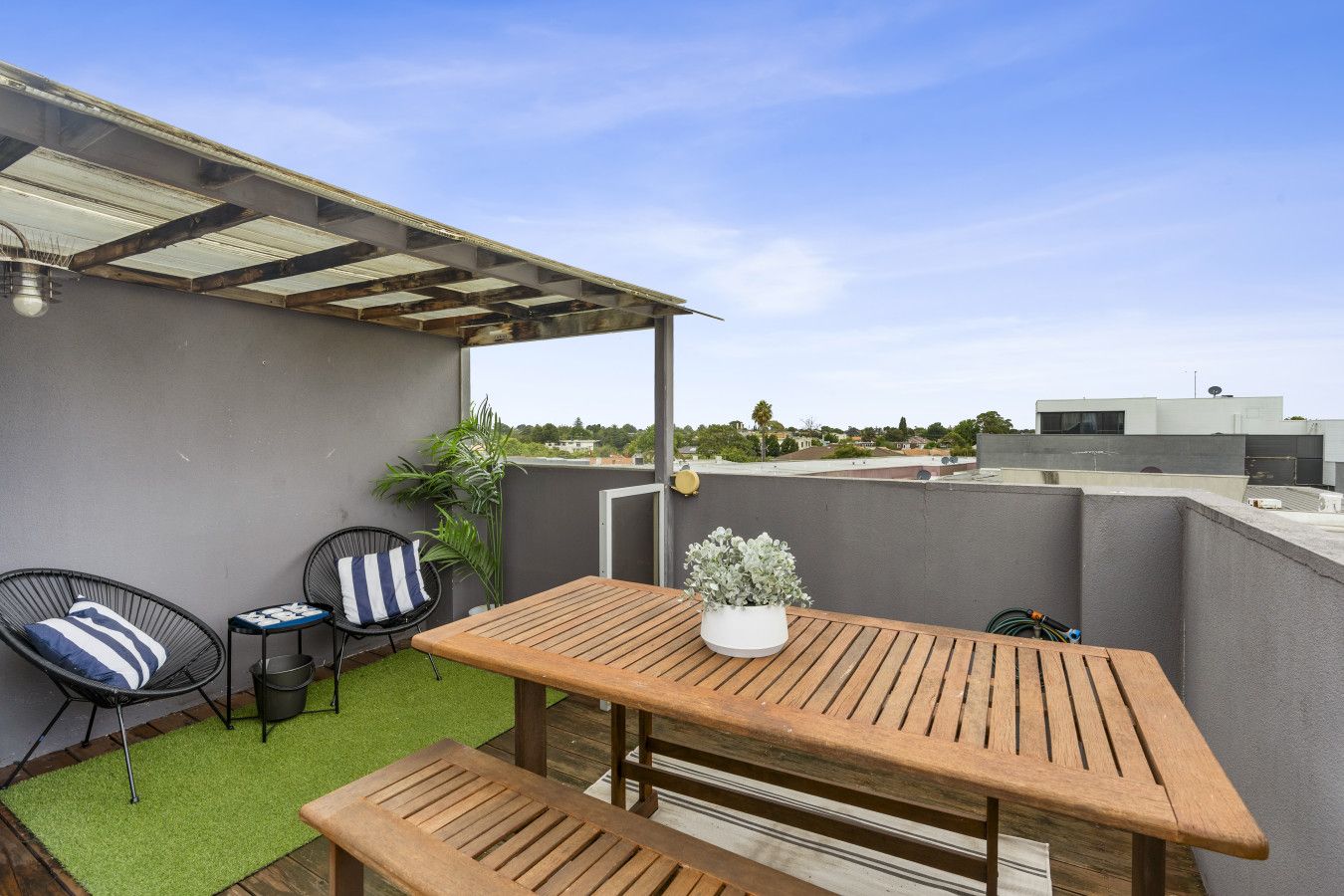 A rooftop patio with a wooden table and chairs, a small potted plant, and a view of the surrounding buildings.