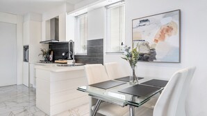 A modern kitchen with white cabinetry, a central island, and a dining area with a glass table and white chairs.