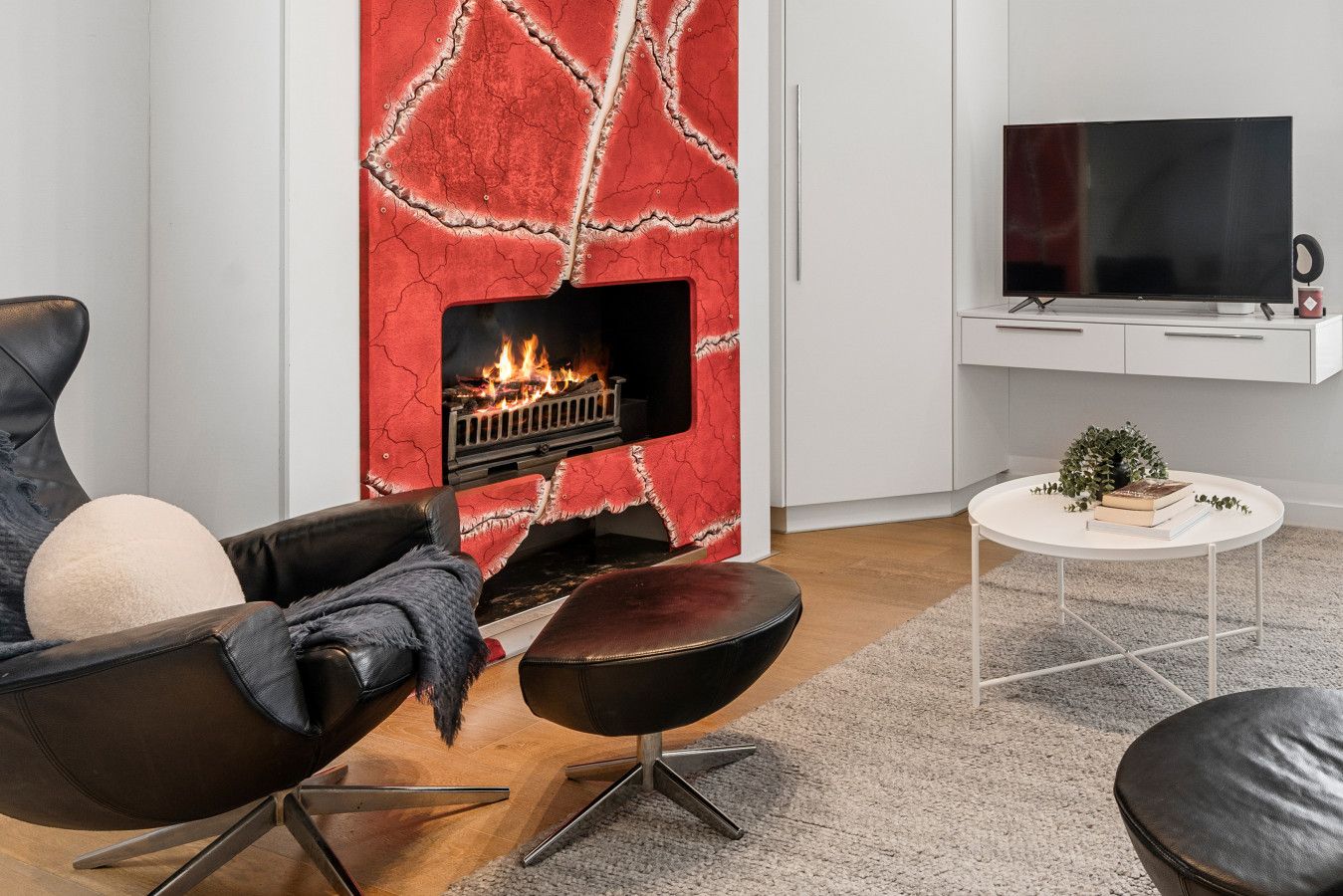 A modern living room with a fireplace, leather furniture, a flat-screen TV, and a small white table with books and a plant.