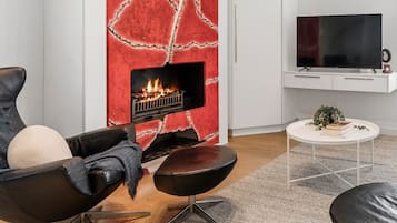 A modern living room with a fireplace, leather furniture, a flat-screen TV, and a small white table with books and a plant.