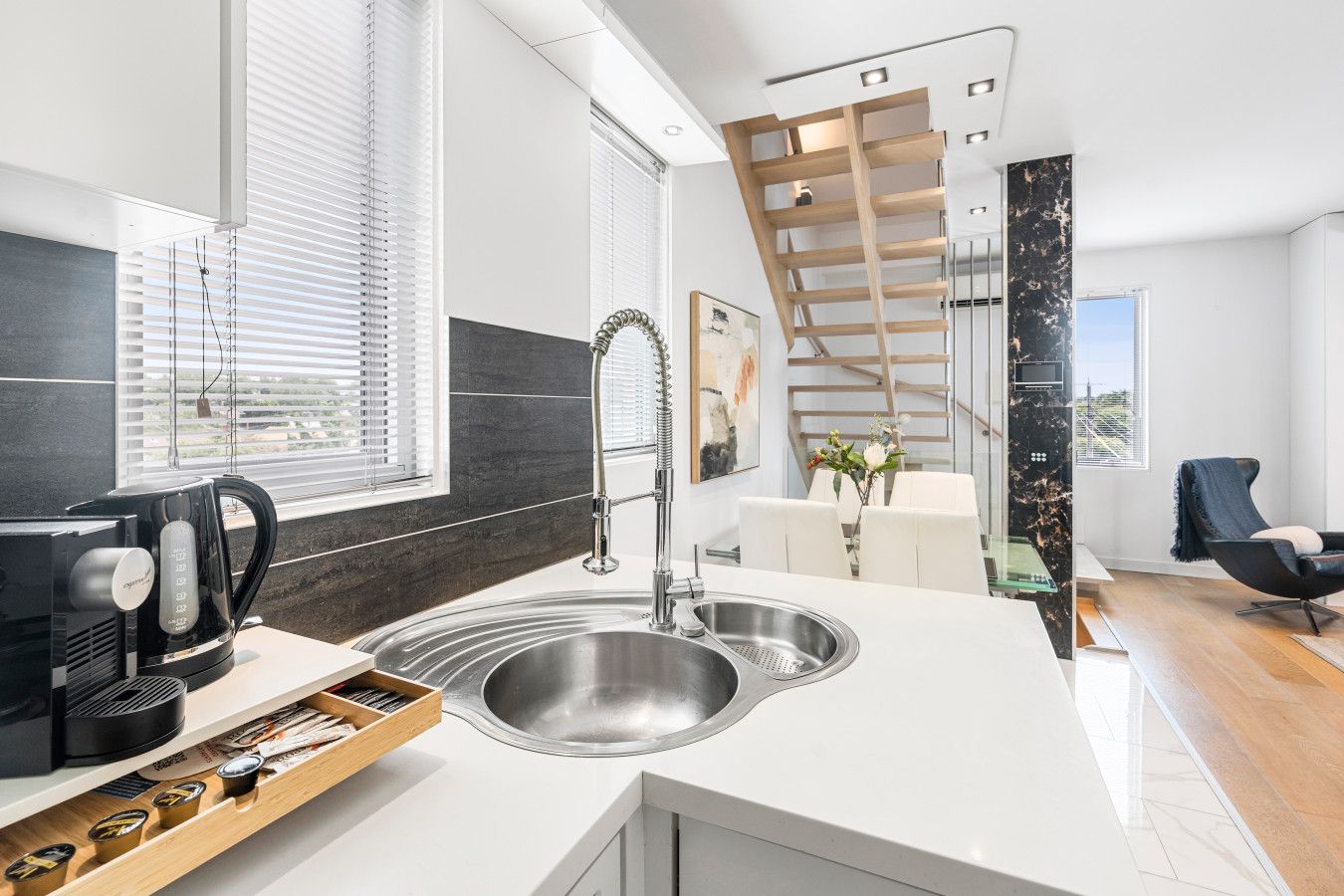 A modern kitchen with a built-in sink, a coffee maker, and a wooden shelf.