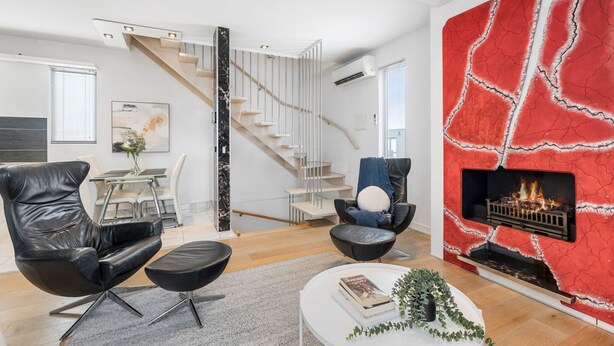 A modern living room with a fireplace, a staircase, and a dining area.