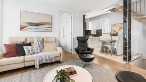 A modern living room with a beige sofa, a black leather chair, and a dining area with a glass table. - The Red Ember Retreat (Caulfield North)