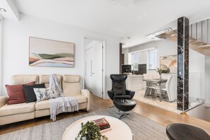 A modern living room with a beige sofa, a black leather chair, and a dining area with a glass table. - The Red Ember Retreat (Caulfield North)