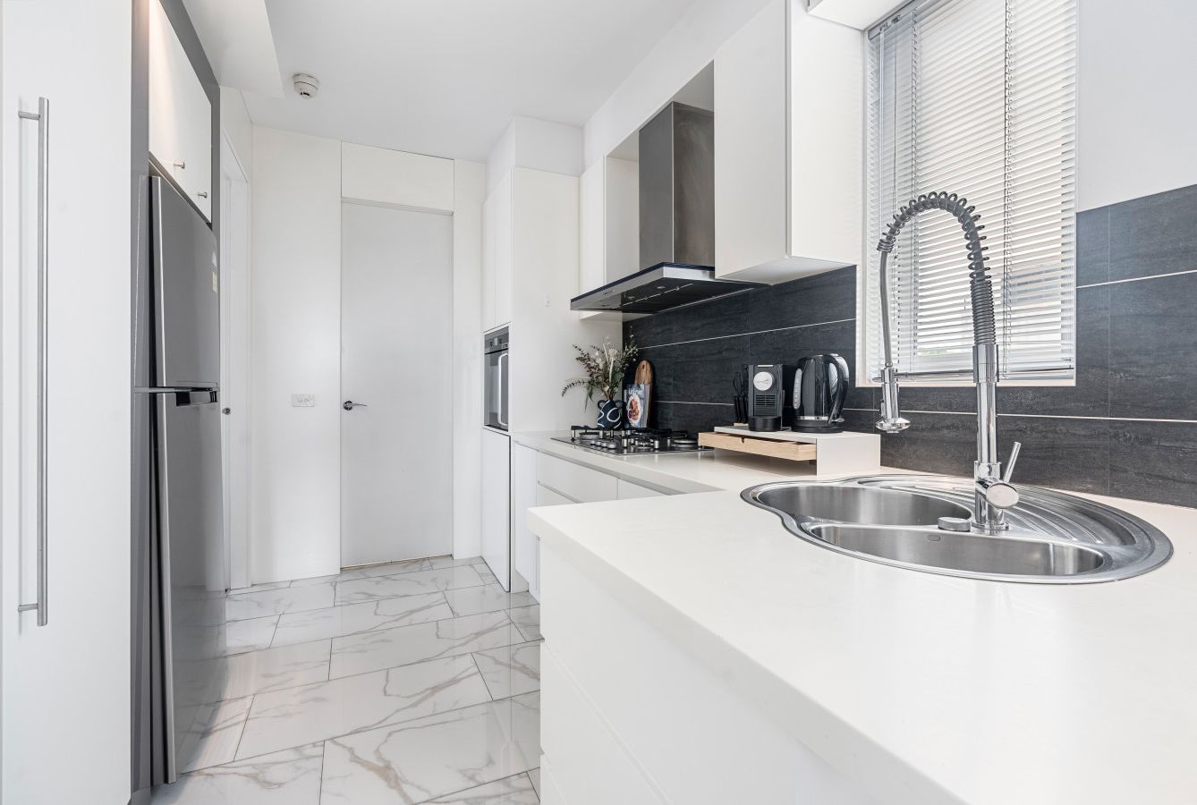 A modern kitchen with a stainless steel sink, a built-in stove, and a black tiled backsplash.