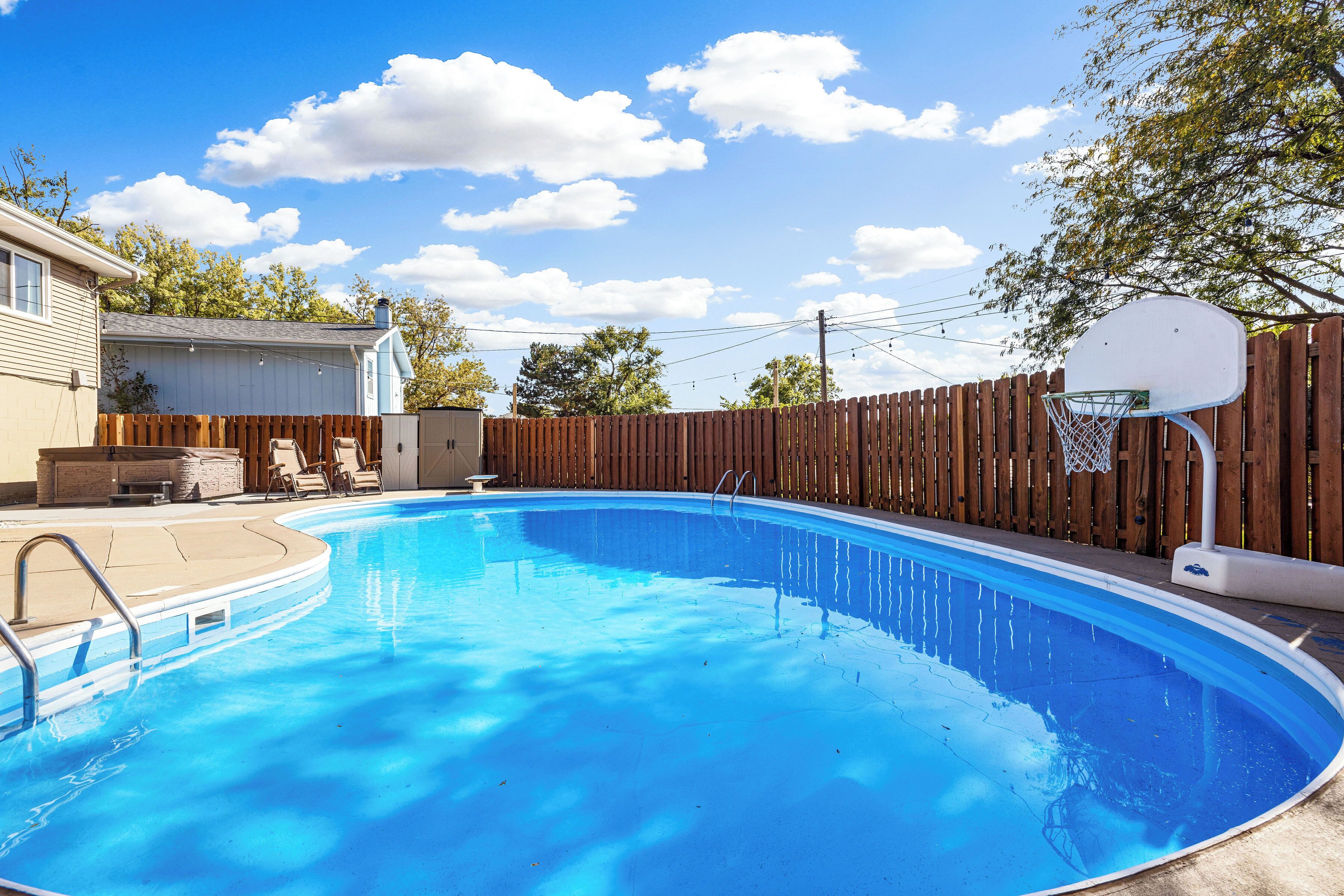 A backyard with a swimming pool, a wooden fence, and a basketball hoop.