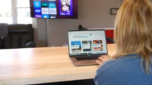 A person using a laptop on a wooden table with a screen displaying a travel website. - Pool, Sauna, Work out area, ping pong, King Bed.  So Many Amenities!!! (Omaha)